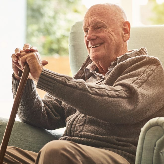 Senior man relaxing in a chair, smiling and holding his cane